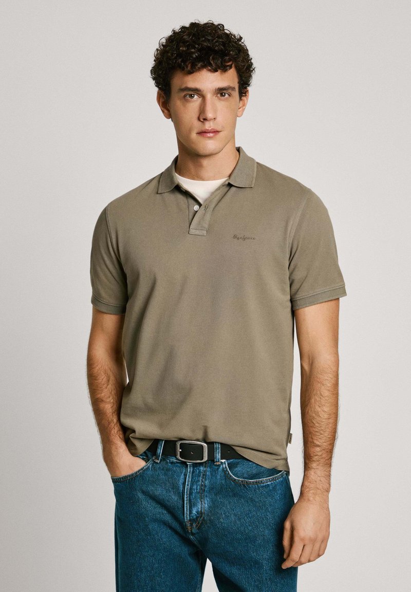 Olivegrøn polo-shirt med krave, korte ærmer og et lille logo. Sammen med blå jeans og et sort bælte. Glat bomuldsstruktur.