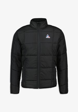 Chaqueta acolchada negra con cuello alto, que cuenta con un cierre frontal, bolsillos laterales y un pequeño logo en la parte superior izquierda. Textura suave.