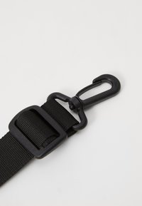 Curea din nailon negru cu cataramă și clip din plastic. Dispune de o suprafață texturată și un sistem de prindere robust pentru o fixare sigură.