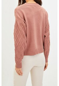 Rosa Pullover mit strukturierten Ärmeln im Rautenmuster und geripptem Saum. Hergestellt aus gewebtem Stoff, mit Rundhalsausschnitt und kürzerer Passform.
