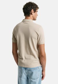 Polo shirt beige a maniche corte realizzato in cotone. Presenta un colletto classico e un design aderente, abbinato a jeans azzurri.