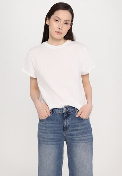 Bela bombažna majica s kroženim ovratnikom in kratkimi rokavi, v kombinaciji z jeans hlačami z visoko pasom v zbledeli modri barvi.