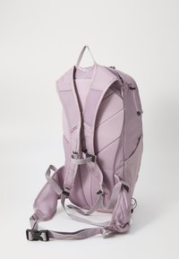 Sac à dos violet clair avec des bretelles rembourrées en mesh, des poches zippées et une forme structurée. Comprend des bretelles réglables et une poignée supérieure.