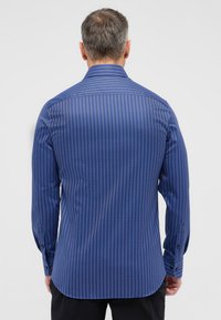 Heren overhemd met lange mouwen in donkerblauw met dunne verticale strepen. Heeft een klassieke kraag, knoopmanchetten en een afgeronde onderkant. Soepele textuur.