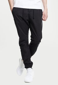 Black tapered joggers made of soft fabric, featuring an elastic waistband with a drawstring, side pockets, and cuffed ankles.