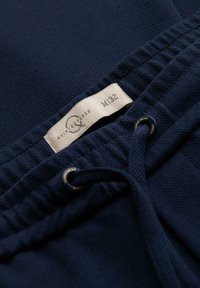 Tissu texturé bleu marine avec taille élastique et cordon de serrage comportant des œillets en métal, et étiquette blanche indiquant M/32.