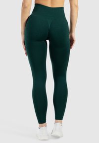 Donkergroene high-waisted leggings met een gladde textuur, een aansluitende pasvorm en een naadloos ontwerp, gecombineerd met witte sport schoenen.