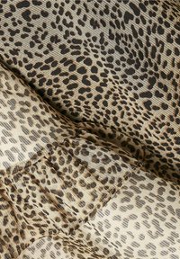 Lepardmönstrad tyg i ljusbeige med bruna och svarta fläckar, med en mjuk, texturerad yta och rynkdetaljer vid sömmen.
