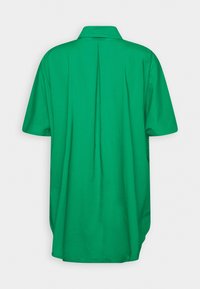 Camicetta verde a maniche corte con colletto, vestibilità rilassata, caratterizzata da una piega sul retro e una texture liscia. Nessun motivo o accento aggiuntivo presente.
