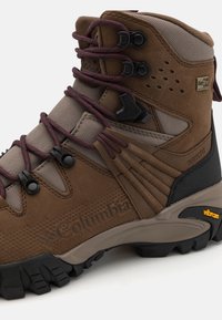 Koffiebruine wandelschoen gemaakt van suede en gaas, met bordeauxrode veters, Vibram-zool, waterdichte OutDry-label en zigzagpatroon op de zijkant.