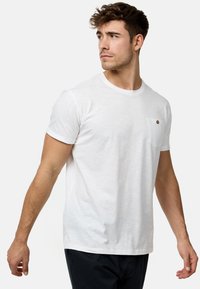 Hvid kortærmet t-shirt med rund halsudskæring, der har en lille lomme og en brun knapdetalje på lommen. Blødt, struktureret materiale.