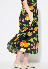 Vestido negro con estampado de frutas y mangas cortas, con naranjas, limones y flores. Combinado con bailarinas de croché en color beige.