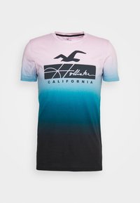 Camiseta de algodón con un diseño degradado de rosa claro a verde azulado oscuro, con un logo gráfico negro que incluye las palabras "Hollister" y "California".