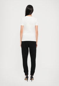 Camisa blanca de manga corta combinada con pantalones de chándal negros. La silueta presenta una parte superior ajustada y una parte inferior relajada, complementada con tacones negros.