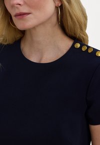 Blusa azul-marinho com decote redondo, apresentando botões decorativos dourados no ombro e uma textura suave.