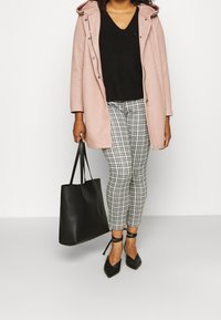 Ljust rosa hooded kappa, svart stickad v-ringad tröja, leggings med hundtandsmönster, svart tote-väska och spetsiga svarta ankelremsklackar.