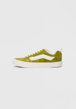 Green suede sneaker with white accents, featuring a low-top design, round toe, and a white rubber sole. Includes laces and a heel tab.