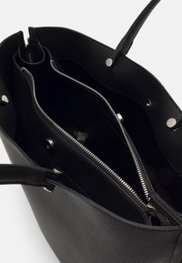 Svart läder tote-väska med en texturerad yta, som har två inre fack, ett med dragkedja, och tryckknappslås på sidorna.