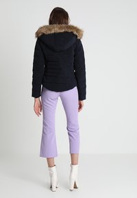 Námořnická prošívaná bunda s kapucí lemovanou kožešinou, prošívanou texturou a střihaným střihem, v kombinaci s levandulovými zkrácenými kalhotami a bílými kotníkovými kozačkami.