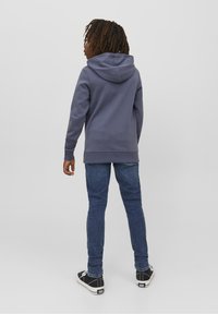 Sudadera con capucha de color gris oscuro y un corte holgado, con puños y dobladillo acanalados. Combinada con vaqueros azules y zapatos negros con acentos blancos.