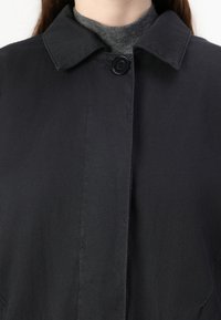 Black collar jacket with a button closure. Textured fabric, straight design. Underneath is a gray turtleneck, partially visible.
