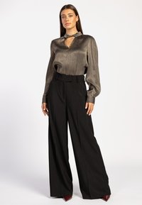 Metalen bronzen blouse met lange mouwen en een keyhole-halssnit, gecombineerd met hoge zwarte wijde broek met een getailleerde pasvorm en een gladde textuur.