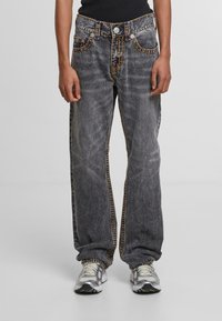 Baggy gray denim jeans with contrasting orange stitching, five pockets, and button closure. Features a straight leg and faded texture.