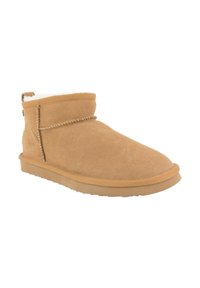 Tan suède enkellaars met een zachte witte fleece voering en een lage rubberen zool. Decoratieve stiksels aan de voorkant en een aantrekband achter.