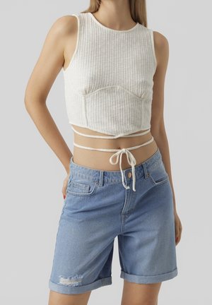 Top corto bianco a coste con un design aderente e dettaglio con laccio laterale, abbinato a pantaloni di jeans azzurri chiari con orlo arrotolato e bordo sfilacciato.