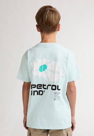 Camiseta de algodón verde menta claro con un diseño gráfico que incluye un óvalo turquesa y líneas de cuadrícula, con el texto audaz en negro "petrol ind". Sin etiquetas visibles.