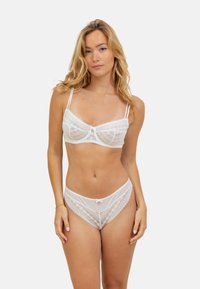 Ensemble de lingerie en dentelle blanche comprenant un soutien-gorge et une culotte, avec des motifs géométriques, des bretelles réglables et des accents en nœud au centre et à la taille.