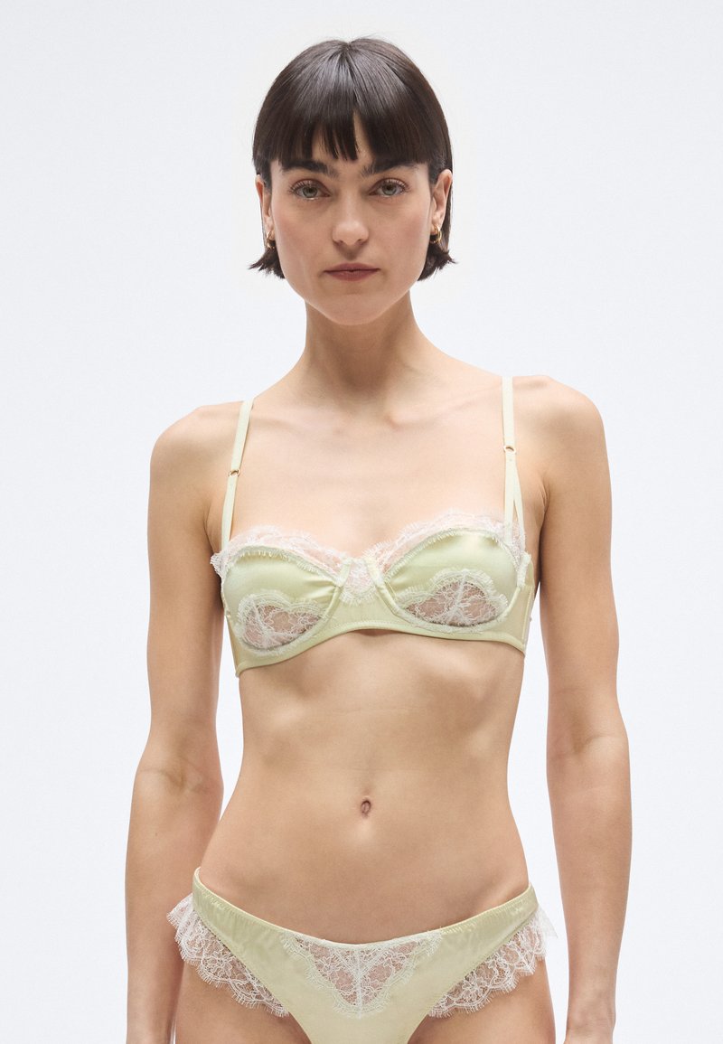 Világoszöld szaténból készült csipkével díszített melltartó és hozzáillő bugyi. A melltartó alátámasztó merevítővel és nyitott csipkepanelekkel rendelkezik; a bugyik csipkebetétes szegéllyel készültek.