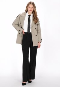 Bézs színű ballonkabát dupla soros gombokkal, fekete nyakkendővel, fehér inggel és fekete, széles szárú nadrággal. Texturált anyag sima felülettel.