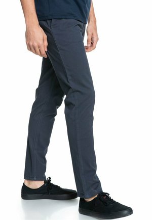 Chinos slim fit gris foncé en tissu lisse, avec poches latérales, lignes épurées, associés à des baskets noires.
