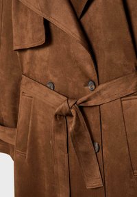 Hnědý suède trench coat s dvouvrstvým designem, páskem v pase a dvěma předními kapsami s odpovídajícími knoflíky. Hladká textura.