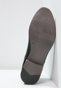 Suela de zapato negro con superficie de goma texturizada, que presenta ranuras horizontales y un tacón plano. El borde es redondeado con un acabado suave.