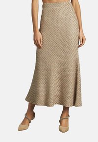 Gonna lunga in maglia beige con un motivo testurizzato, che si allarga dolcemente dalla vita all'orlo, abbinata a scarpe con tacco beige.