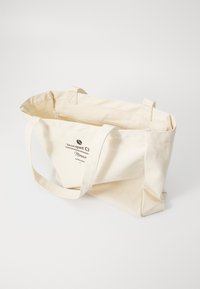 Plátená taška v off-white farbe s dvoma pevným ušami. Na jednej strane má potlačené logo a text. Jednoduchý, obdĺžnikový dizajn.