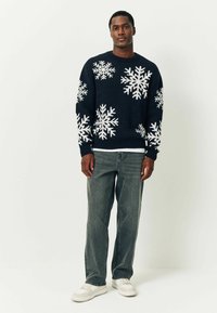 Maglione blu navy con motivo di fiocchi di neve bianchi, collo rotondo e polsini a costine, abbinato a jeans grigi e sneakers bianche.