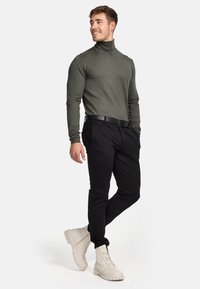Grüner Rollkragenpullover kombiniert mit schwarzen Hosen und beigen Schnürstiefeln. Der Stoff ist glatt und der Schnitt ist tailliert.