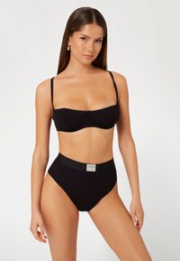 Crni bikini set koji se sastoji od bandeau topa s tankim trakama i gaćica s visokim strukom. Rebrasta tekstura s logom na pojasu.