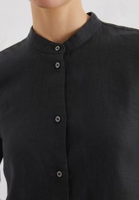 Zwarte linnen shirt met een mandarin-kraag, voorpaneel met vijf grijze knopen en een gestructureerde stofoppervlak.