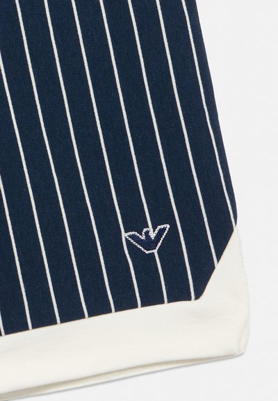 Tela azul marino con finas rayas verticales blancas, pequeño logotipo bordado de un pájaro en blanco y azul marino cerca del borde inferior, detalle de dobladillo blanco.