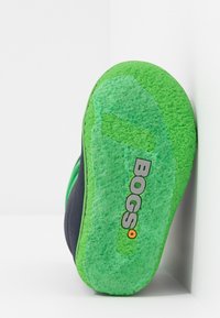 Zielona gumowa podeszwa buta Bogs, z fakturowaną powierzchnią i czarną cholewką, z wyraźnie widocznym logo "BOGS".