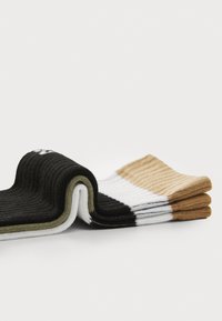 Quatre paires de chaussettes côtelées empilées, présentant des couleurs noir, blanc, vert olive et beige avec des poignets contrastés et une finition texturée.