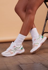 Baskets de sport blanches avec des accents roses, verts et beiges, dotées d'un dessus en mesh, d'une semelle chunky et d'un logo sur le côté.