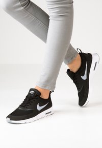 Svarta Nike-sneakers med överdel i mesh, vit mellansoffa och grå detaljer. Med snören och en framträdande swoosh-logotyp på sidan.