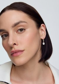 Złote kolczyki w kształcie kół z przezroczystym kamieniem z cubic zirconia, cechujące się gładką teksturą i minimalistycznym designem.