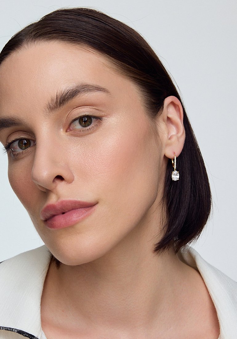 Złote kolczyki w kształcie kół z przezroczystym kamieniem z cubic zirconia, cechujące się gładką teksturą i minimalistycznym designem.