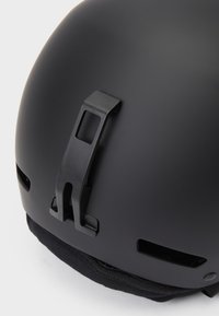 Černá helma s matným povrchem, vybavená zadním zajišťovacím klipem, větracími otvory a měkkým černým podšívkou na bázi.